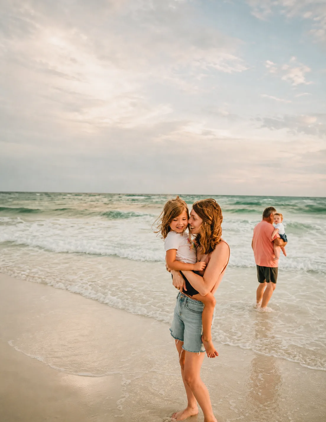 A parent and two children walking together at the shoreline at golden hour